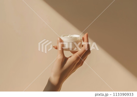 Female hand holding jar of cosmetic cream jar on pastel beige neutral background. Pair of beautiful girl hands with blank mockup tube of cream. Daily skincare and body care routine. Branding mock up. Female hand holding jar of cosmetic cream jar on pastel beige neutral background. Pair of beautiful girl hands with blank mockup tube of cream. Daily skincare and body care routine. Branding mock up. 113390933