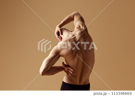 Rear view of bald man with muscular build body stretching his neck, highlighting strong physique against beige studio background. Rear view of bald man with muscular build body stretching his neck, highlighting strong physique against beige studio background. 113396669