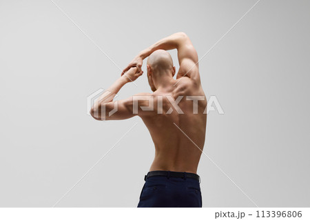 Rear view of sculpted physique of young bald man with beard in power stance against grey studio background. Rear view of sculpted physique of young bald man with beard in power stance against grey studio background. 113396806