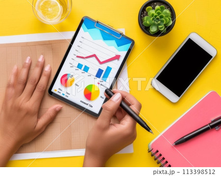 Overhead view of hands reviewing colorful growth charts on a digital tablet 113398512
