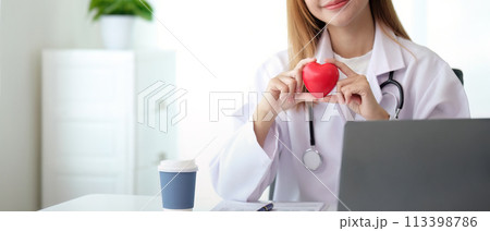 Happy young doctor woman holding red heart shape object, looking at camera with smile. Positive practitioner, cardiologist 113398786