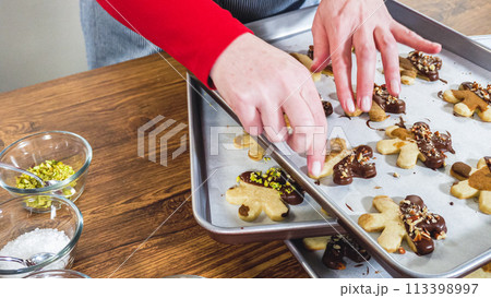 Carefully packaging Christmas cutout cookies, half-dipped in chocolate and presented in clear cellophane wrapping, perfect for festive gifting. 113398997