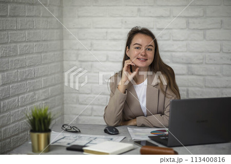 Manager Moment: A snapshot of success as a vibrant young businesswoman smiles, fully engaged with her work in a modern office 113400816