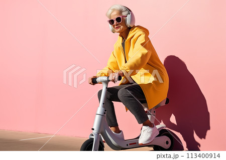 Smiling happy cool gray haired old senior woman on scooter moves on pink background. Older people freedom spirit concept Smiling happy cool gray haired old senior woman on scooter moves on pink background. Older people freedom spirit concept 113400914