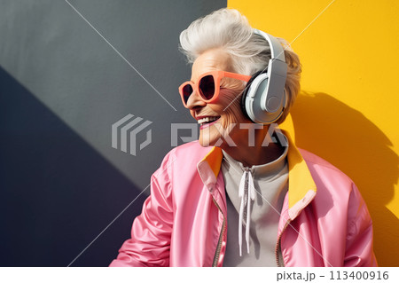 An elderly woman in sunglasses listens to music with headphones outdoors 113400916