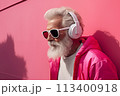 An elderly man in sunglasses listens to music with headphones outdoors 113400918