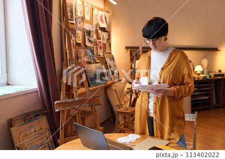 Waist up portrait of female business owner sorting bills and taxes while managing finances in art studio, copy space 113402022