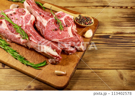 Raw fresh beef rib eye steak on bone with spices, garlic and rosemary on wooden table 113402578