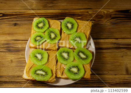 Tasty sandwiches with peanut butter and kiwi fruits on wooden table. Top view 113402599