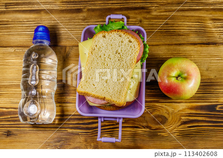 Lunch box with sandwiches, bottle of water and apple on a wooden table. Top view Lunch box with sandwiches, bottle of water and apple on a wooden table. Top view 113402608