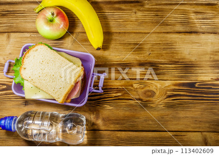Lunch box with sandwiches, bottle of water, banana and apple on a wooden table. Top view, copy space Lunch box with sandwiches, bottle of water, banana and apple on a wooden table. Top view, copy space 113402609