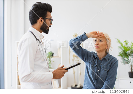 Respected man doctor and senior woman patient sitting at exam couch. 113402945