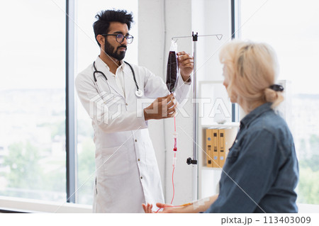 Elderly woman receiving blood transfusion looking at medical doctor. Elderly woman receiving blood transfusion looking at medical doctor. 113403009