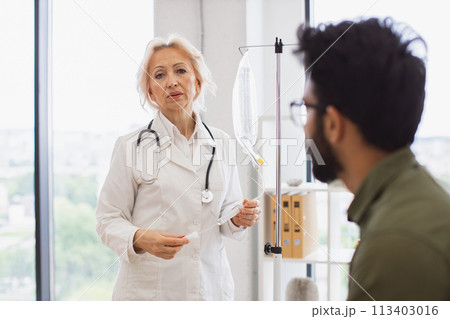 Elderly woman in lab coat testing dropper with solution for chemotherapy. Elderly woman in lab coat testing dropper with solution for chemotherapy. 113403016