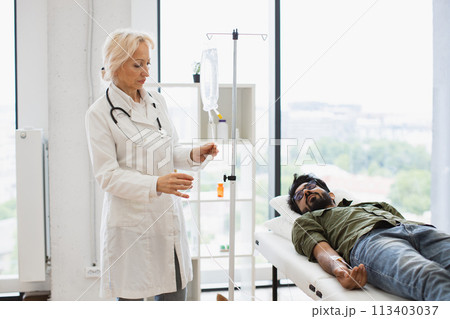 Bearded young man receiving chemotherapy looking at nurse in lab coat. Bearded young man receiving chemotherapy looking at nurse in lab coat. 113403037