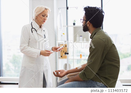 Bearded man receiving chemotherapy looking at nurse preparing a dropper. Bearded man receiving chemotherapy looking at nurse preparing a dropper. 113403572