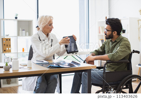 Senior specialist discussing results of diagnostic tests with wheelchair user. Senior specialist discussing results of diagnostic tests with wheelchair user. 113403626
