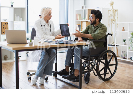 Senior lady demonstrating spine scans on tablet to mindful man using wheelchair Senior lady demonstrating spine scans on tablet to mindful man using wheelchair 113403636
