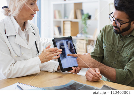 Skilled radiologist in white uniform explaining visible changes on x-ray image. Skilled radiologist in white uniform explaining visible changes on x-ray image. 113403802
