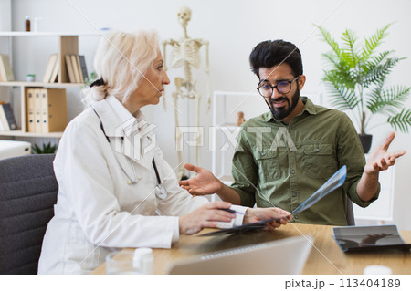 Skilled radiologist in white uniform explaining visible changes on x-ray image Skilled radiologist in white uniform explaining visible changes on x-ray image 113404189