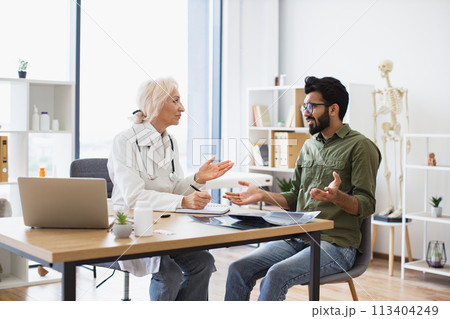 Gentleman describing symptoms of illness to senior female doctor. 113404249