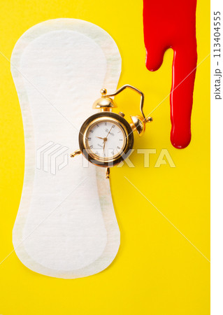 Blood, alarm clock and feminine hygiene pad with red glitter on yellow background. First menstrual period concept 113404555
