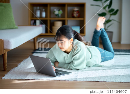 部屋でうつ伏せに寝転んでパソコンを操作する私服の若い女性 113404607