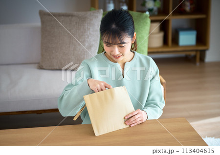 自宅でメール便の荷物を確認する若い私服の女性 自宅でメール便の荷物を確認する若い私服の女性 113404615