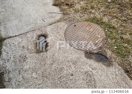 A rusty iron hatch with a pattern with a large gap at the top is mounted in the asphalt pavement of the pedestrian road. Close-up 113406016