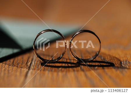 Two golden wedding rings stand together on wooden table. Sun shines on rings. Shadow from rings 113406127