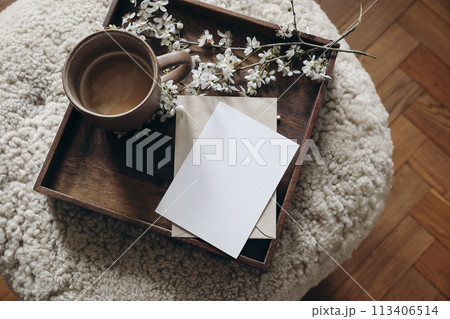 Spring still life composition. Greeting card mockup, cup of coffee. Feminine photo. Floral scene. Blurred cherry tree blossoms on wool taburet, stool. Defocused wooden parquet floor. Top view. Spring still life composition. Greeting card mockup, cup of coffee. Feminine photo. Floral scene. Blurred cherry tree blossoms on wool taburet, stool. Defocused wooden parquet floor. Top view. 113406514