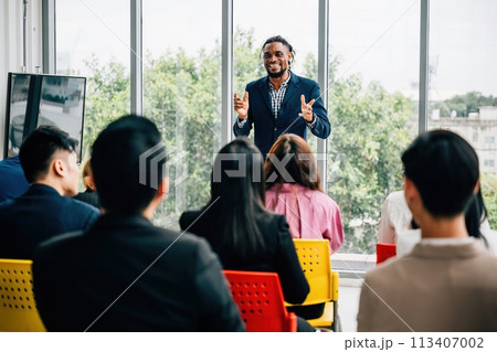 A diverse group of businesspeople convenes in an office meeting. Seated colleagues exchange thoughts, while male and female managers stand, promoting effective teamwork. 113407002
