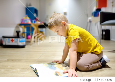 Cute little boy reading a book on the floor in a kindergarten. The child has time in the preschool 113407380