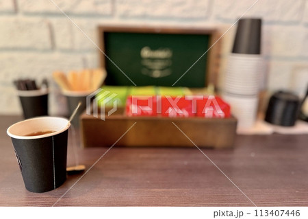 Box with different types of black and green tea and carton cup is located on a wooden table. Free tea drinking area in the car dealership for customers 113407446
