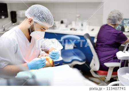 Dentist and patient at modern medical center. Doctor treats a young woman teeth in hospital. Practitioner examines the patient before orthodontists or prosthetics treatment. Dentist and patient at modern medical center. Doctor treats a young woman teeth in hospital. Practitioner examines the patient before orthodontists or prosthetics treatment. 113407741