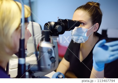 Slit Lamp eye examination with ophthalmologist. Patient during visit by oculist for exam of biomicroscopic analysis of eyelids, sclera, conjunctiva, iris, lens, cornea. Checkup of retina and fundus Slit Lamp eye examination with ophthalmologist. Patient during visit by oculist for exam of biomicroscopic analysis of eyelids, sclera, conjunctiva, iris, lens, cornea. Checkup of retina and fundus 113407794