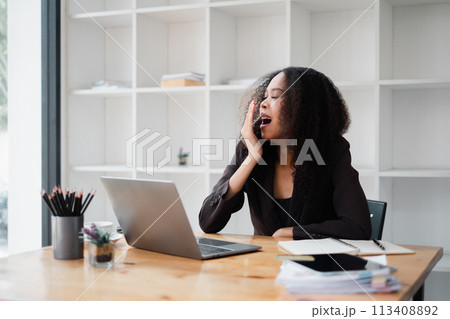 Overwhelmed businesswoman holds her head in distress while working on a laptop at her desk in a contemporary office. 113408892