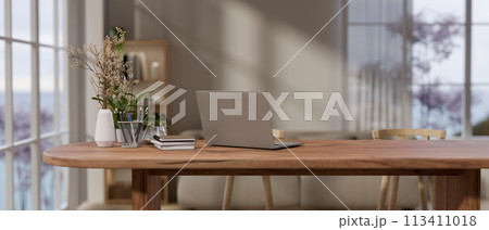 A laptop computer and decor on a wooden table by the window in a cozy contemporary room. 113411018