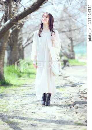 桜並木の河川敷を歩く女性 113414534