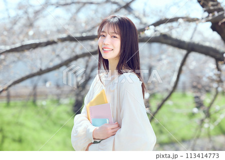 桜並木の河川敷を歩く女性 113414773