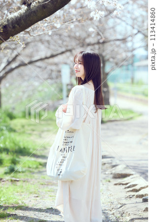 桜並木の河川敷を歩く女性 113414860
