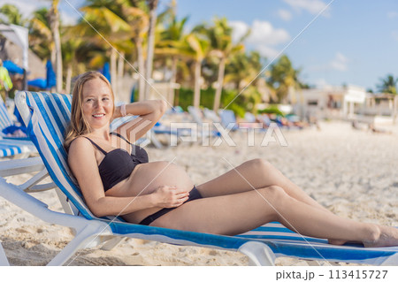 Basking in seaside tranquility, a pregnant woman lounges on a sun lounger, embracing the soothing ambiance of the beach for a moment of serene relaxation 113415727