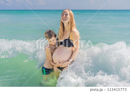 A picturesque moment: a pregnant woman and her son enjoying the turquoise sea, a heartwarming family bond by the tranquil shore 113415773