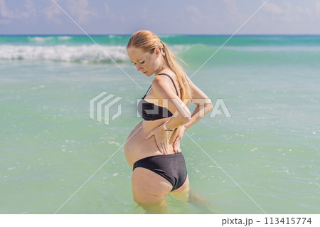 In the sea, a pregnant woman experiences a moment of discomfort as she stands, gently tending to her back, highlighting the challenges of back pain during pregnancy In the sea, a pregnant woman experiences a moment of discomfort as she stands, gently tending to her back, highlighting the challenges of back pain during pregnancy 113415774