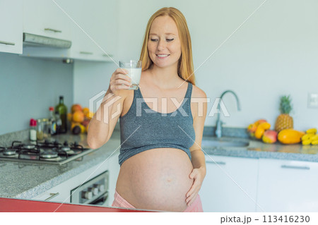 Weighing the pros and cons of milk during pregnancy, a thoughtful pregnant woman stands in the kitchen with a glass, contemplating the decision to include or avoid milk for her and her baby's well 113416230