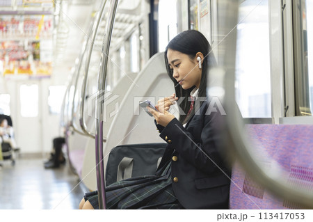 電車の中でスマートホンの画面を見るイヤホンをつけた女子高校生　電車通学　イメージ 113417053