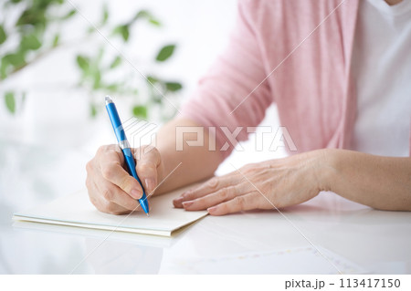手紙を書くミドル女性の手元 113417150