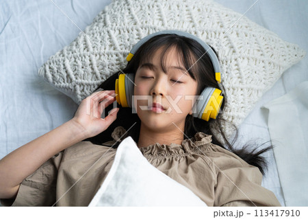 ヘッドフォンをしてベッドで寝ている女の子 113417910