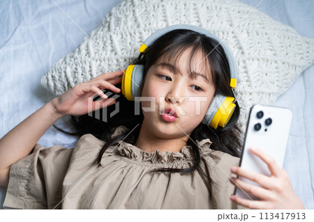 ヘッドフォンをしてベッドでスマホを操作する女の子 ヘッドフォンをしてベッドでスマホを操作する女の子 113417913