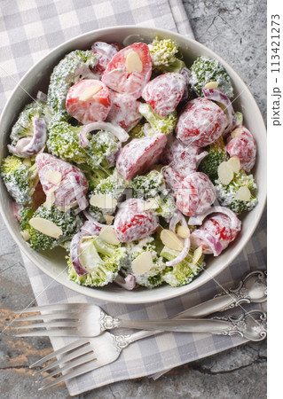 Homemade diet broccoli salad with fresh strawberries, red onions, almonds and Greek yogurt close-up in a plate on the table. Vertical top view 113421273